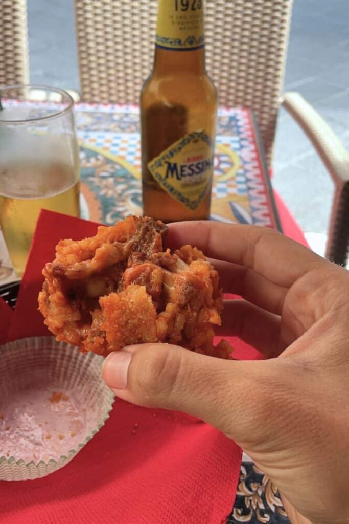 Eating arrancini and drinking Italian beer between beach and mountain time on the Sicily road trip.